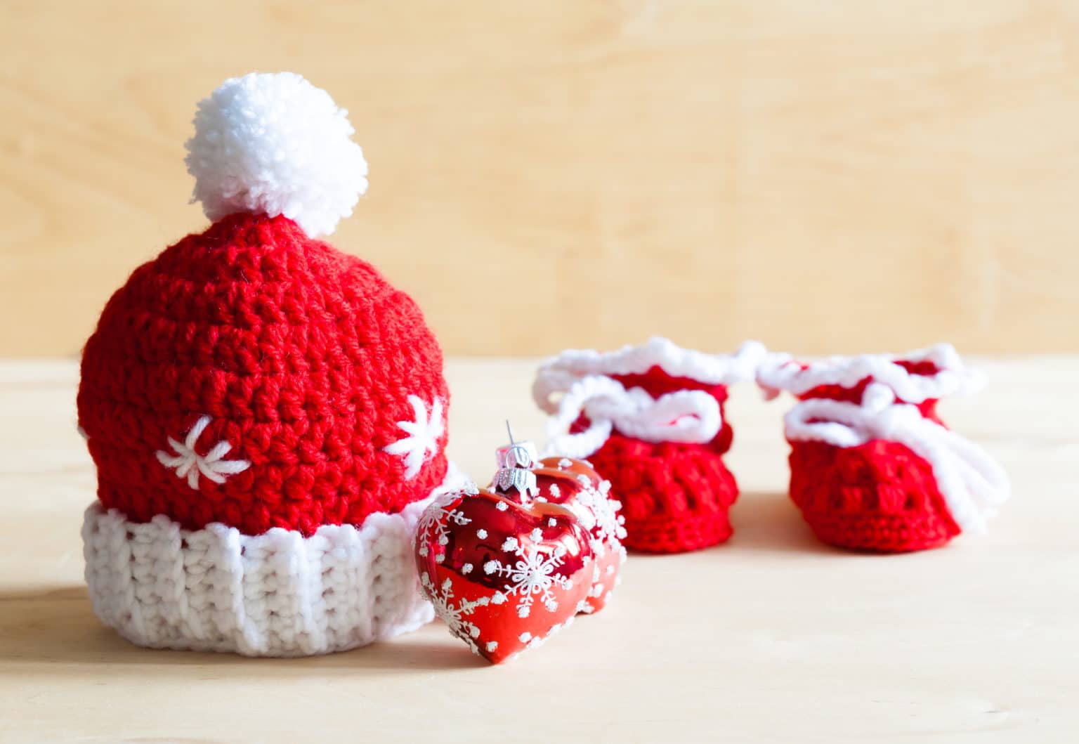 Beautiful Christmas background. Knitting red hat, tree toy, baby's bootees. Woman knits hands. Crochet hook handmade. Woolen thread. Close up. Winter event.